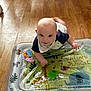 baby, infant, tummy_time, inflatable_mat, jungle_theme, animal_prints, wooden_floor, indoors, child, playtime, colorful, curious, smiling, cute, young_child, blue_shirt, bib, floor_play, giraffe, elephant
