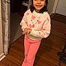 child, girl, smiling, indoors, portrait, standing, pink_clothing, sweater, heart_pattern, necklace, bracelet, fashion, wood_floor, doorway, curtain, home, shoes, jewelry, happy, full_body