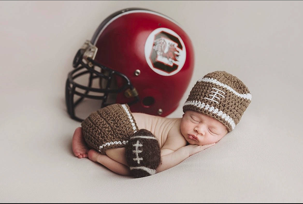 Fisher is registered to the contest to win money with this photo: baby, baby_toddler_clothing, cap, comfort, creative_arts, fashion_accessory, font, head, headgear, headwear, helmet, knit_cap, linens, magenta, pattern, person, personal_protective_equipment, sports_equipment, sports_gear, toddler