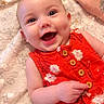 baby, smiling, infant, red_dress, floral_pattern, blanket, hand, tattoo, nail_polish, happy, cute, portrait, lying_down, close_up, sparkle_effect, dimples, skin, child, joy, soft_texture