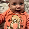 Isabella joined the competition — help win amazing prizes! baby, smiling, onesie, teddy_bear, orange_clothing, infant, happy, face, closeup, child, cute, blanket, pattern, soft_texture, portrait, young_child, expression, indoors, cuddly, adorable