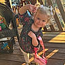 Everleigh joined the competition — help win amazing prizes! toddler, child, pigtails, bows, pink_purse, floral_top, white_leggings, gold_sandals, wooden_porch, sunlight, outdoor, playful, smiling, chair, string_lights, wooden_railing, happy, person, daylight, cute