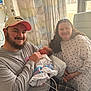 Kennedy is registered to the contest to win money with this photo: newborn, baby, hospital, family, father, mother, smile, hospital_gown, blanket, curtains, window, medical_equipment, beard, hat, plaid_pants, indoor, person, holding, love, parenthood
