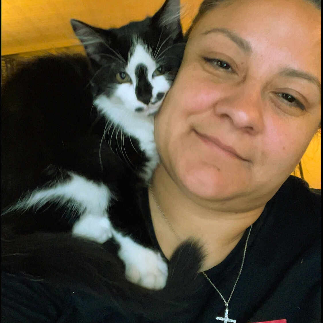 Pepper is registered to the contest to win money with this photo: woman, cat, black_and_white_cat, shoulder, portrait, smile, jewelry, cross_necklace, indoor, closeup, feline, pet, face, happy, casual_clothing, black_shirt, relaxation, cozy, companion, warm_lighting