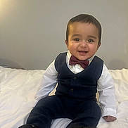 Najaf is registered to the contest to win money with this photo: baby, bed, bow_tie, child, clothing, cute, face, fashion, happy, head, indoors, pants, person, portrait, shoes, sitting, smiling, vest, white_shirt, young