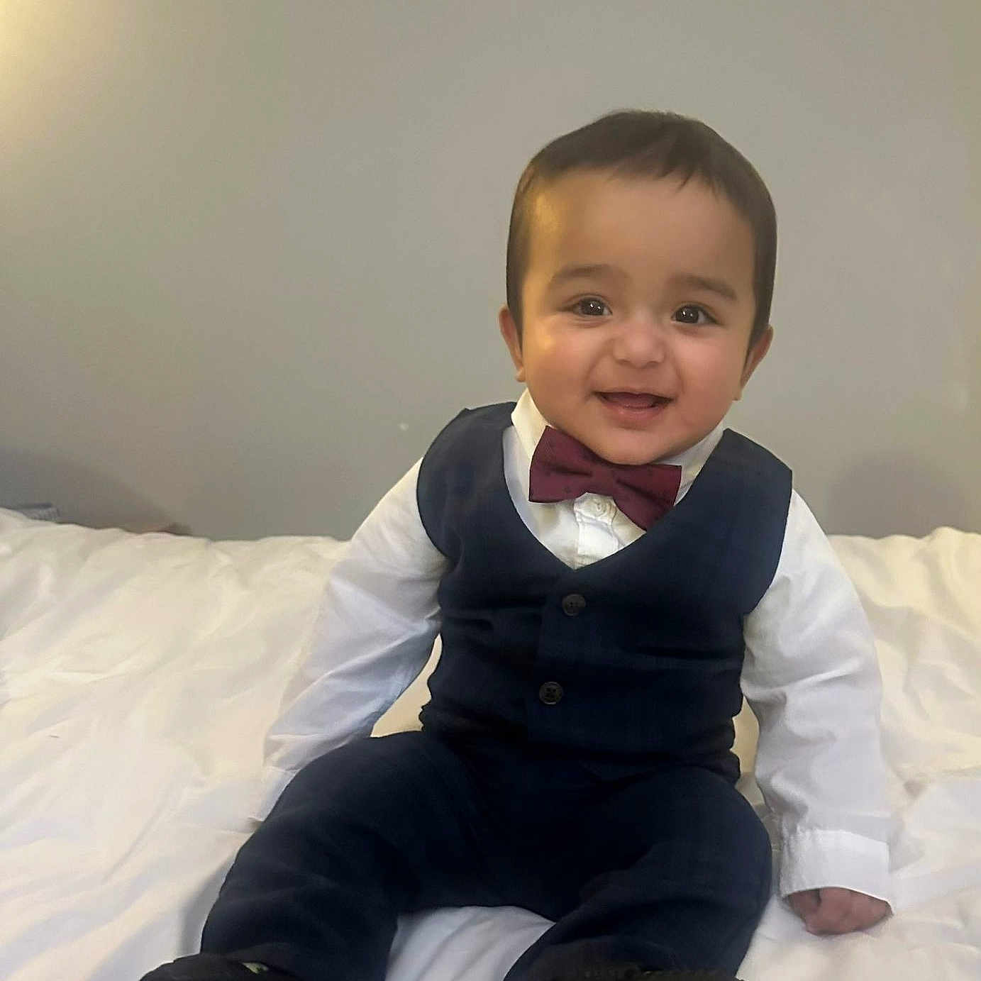 Najaf is registered to the contest to win money with this photo: baby, bed, bow_tie, child, clothing, cute, face, fashion, happy, head, indoors, pants, person, portrait, shoes, sitting, smiling, vest, white_shirt, young