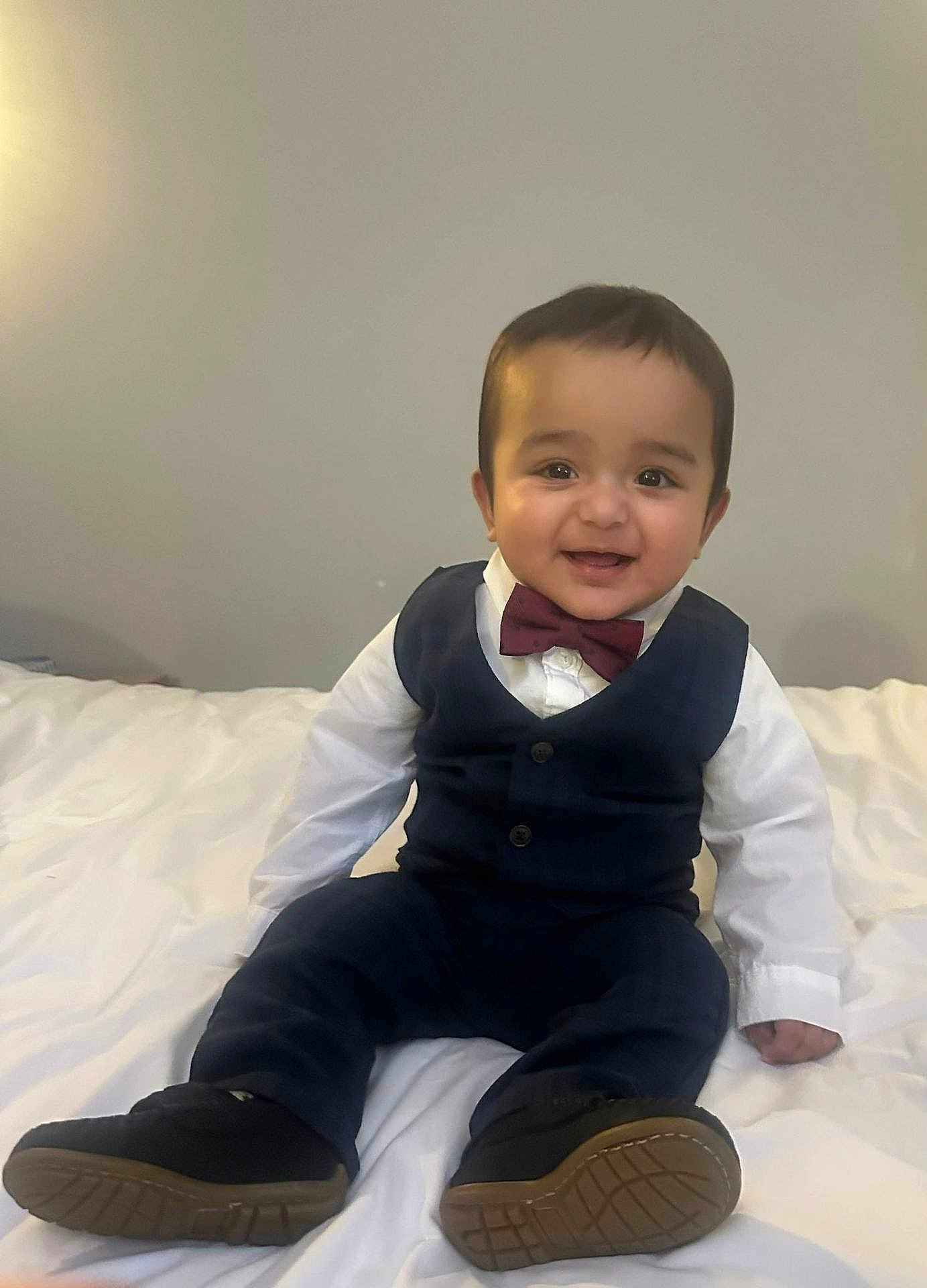 Najaf is registered to the contest to win money with this photo: baby, bed, bow_tie, child, clothing, cute, face, fashion, happy, head, indoors, pants, person, portrait, shoes, sitting, smiling, vest, white_shirt, young