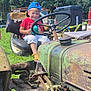 Angelo a rejoint le concours — aidez-le/la à gagner de superbes lots ! child, boy, smiling, blue_cap, red_shirt, tractor, steering_wheel, seat, grass, forest, vintage_tractor, sandals, sippy_cup, rust, machinery, outdoor_event, vehicle, happy, portrait, playtime