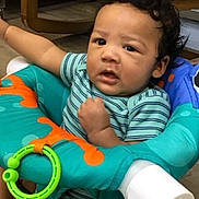 Jasai joined the competition — help win amazing prizes! baby, child, infant, baby_seat, toy, colorful, indoor, furniture, curly_hair, striped_clothing, floor, expression, face, person, seat, hand, play, young, cute, looking