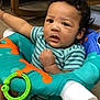 baby, child, infant, baby_seat, toy, colorful, indoor, furniture, curly_hair, striped_clothing, floor, expression, face, person, seat, hand, play, young, cute, looking