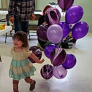 Evelyn is registered to the contest to win money with this photo: adult, baby, balloons, boots, bottle, car_seat, celebration, chair, dress, floor, indoor, leggings, marbled, party, plaid_shirt, purple, smile, table, toddler, window