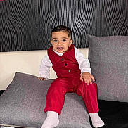 Alessyo a rejoint le concours — aidez-le/la à gagner de superbes lots ! toddler, child, red_outfit, cushion, gray_pillow, indoor, smiling, face, person, baby_toy, white_socks, seated, black_background, textured_wall, home, cute, fashion, portrait, young_child, furniture