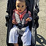 baby, child, stroller, outdoor, sunlight, pavement, curious, pink_shirt, white_pants, barefoot, seatbelt, infant, person, portrait, daylight, expression, casual_clothing, walking, shadow, urban