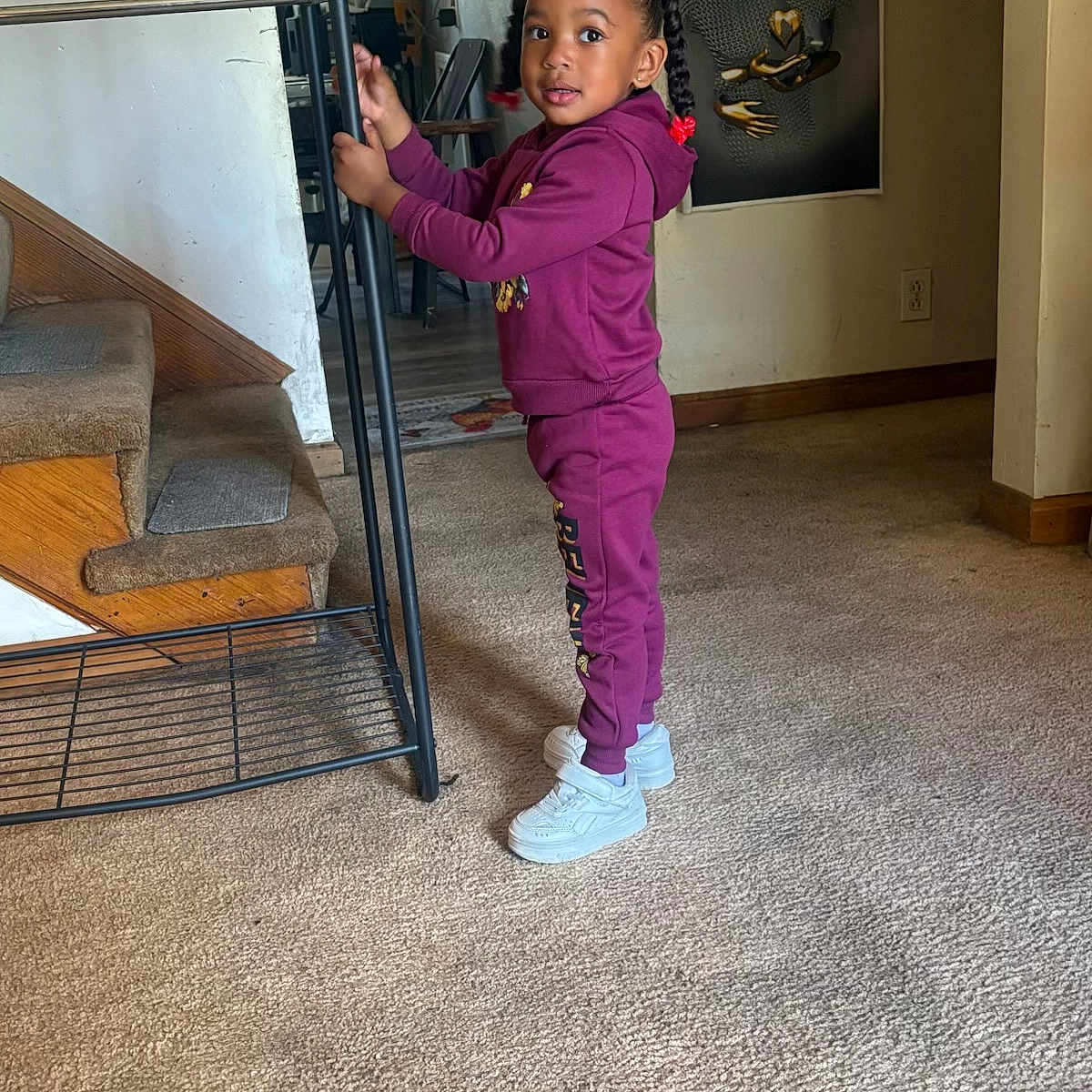 Tayana Grier joined the competition — help win amazing prizes! braids, bright_eyes, carpet, casual_clothing, child, curious, floor, girl, hair_beads, home, indoor, metal_rack, portrait, purple_tracksuit, room, stairs, standing, wall_art, white_shoes, young_child