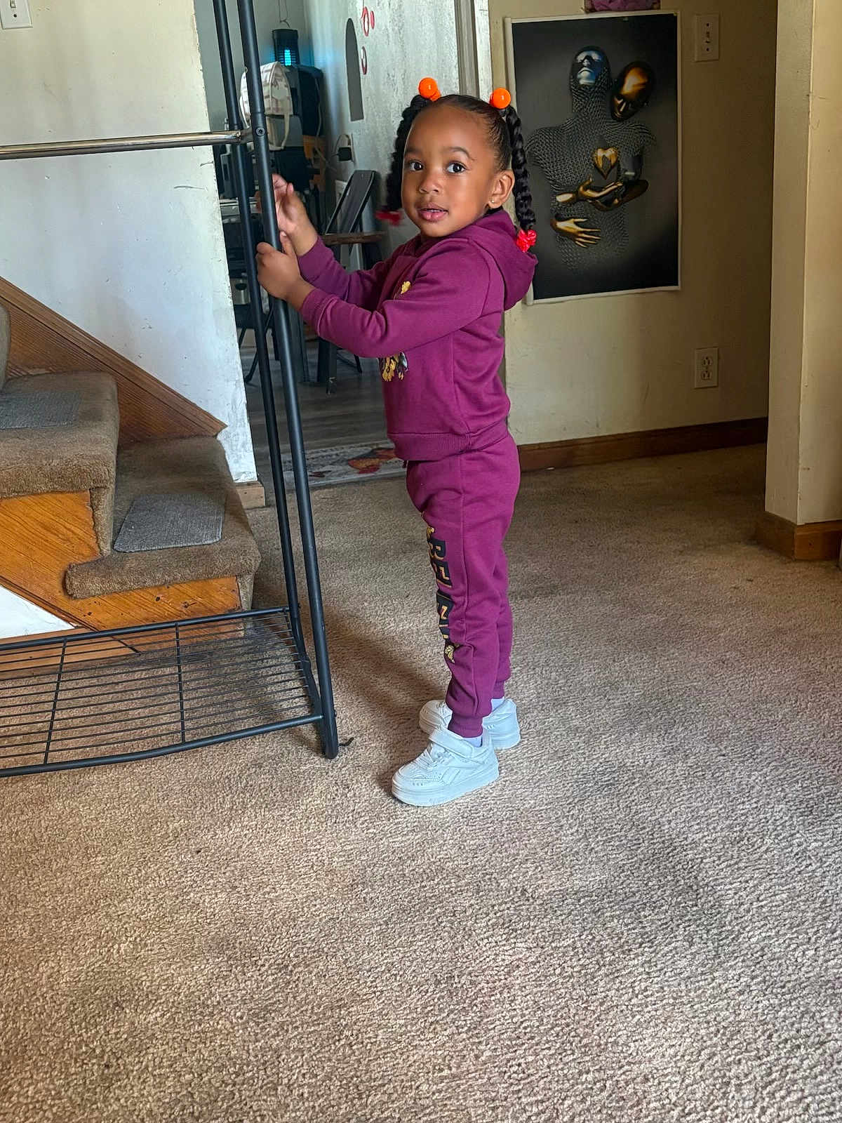 Tayana Grier joined the competition — help win amazing prizes! child, girl, indoor, carpet, stairs, braids, purple_tracksuit, white_shoes, metal_rack, wall_art, curious, standing, floor, home, bright_eyes, hair_beads, casual_clothing, young_child, portrait, room
