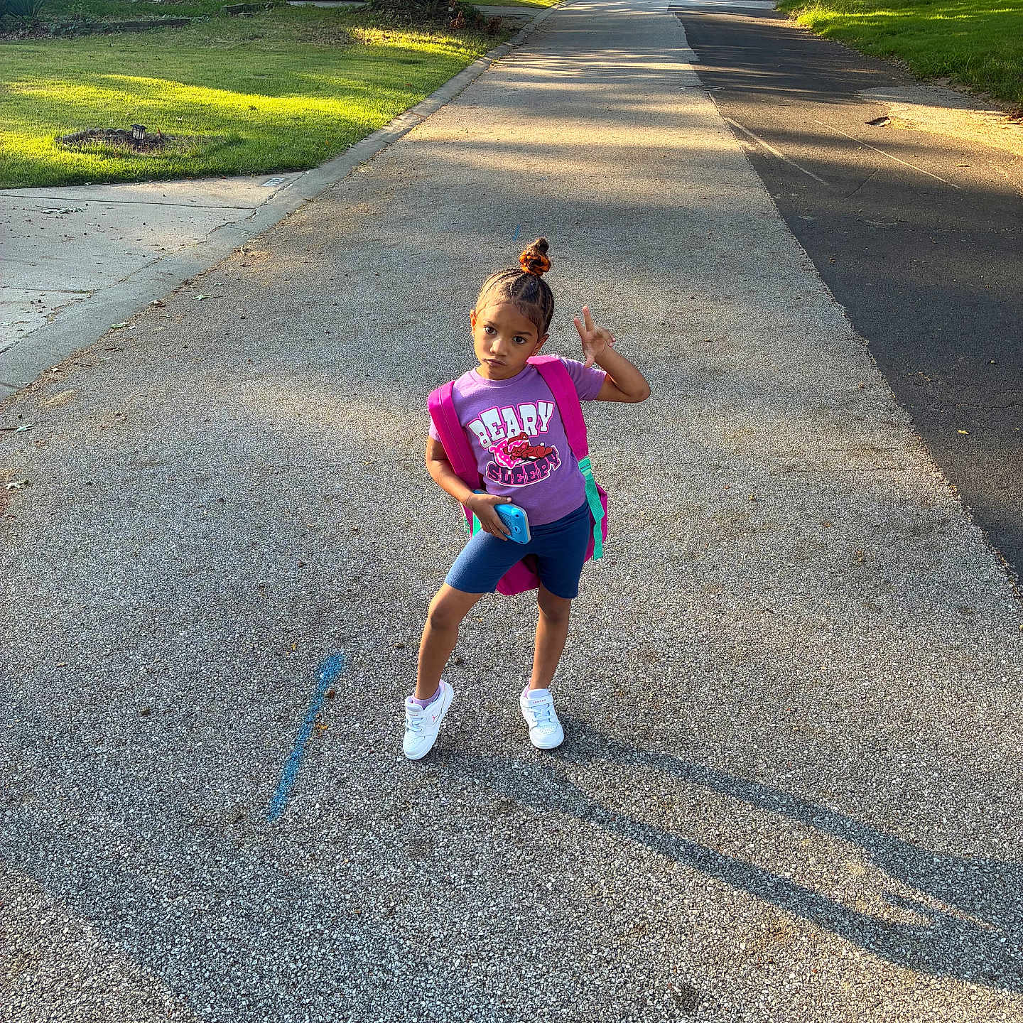 Donna joined the competition — help win amazing prizes! child, street, pose, purple_shirt, shorts, sneakers, backpack, sidewalk, shadow, tree, grass, residential_area, house, car, sunlight, afternoon, playful, outdoor, person, phone