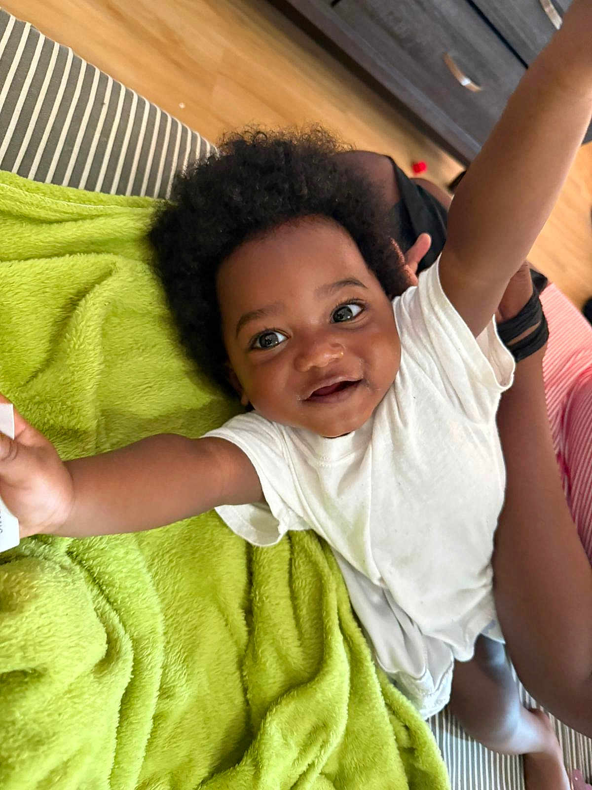 Shemar joined the competition — help win amazing prizes! toddler, child, smiling, happy, arms_up, curly_hair, white_shirt, green_blanket, striped_couch, wooden_floor, indoor, person, baby, cute, playful, face, skin, expression, joy, home