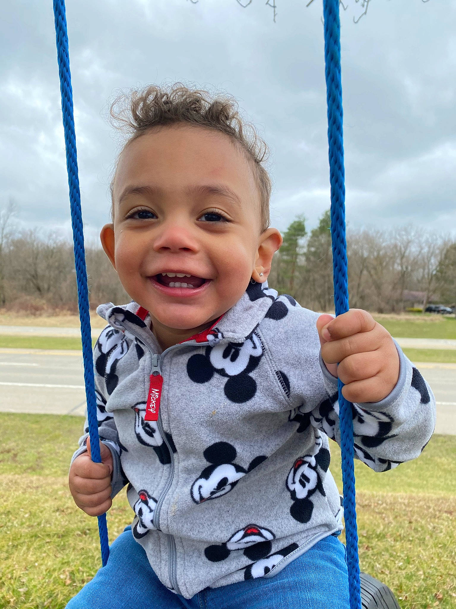 Brayson is registered to the contest to win money with this photo: baby_toddler_clothing, cloud, eye, face, gesture, grass, happy, human_body, joy, leisure, outdoor_play_equipment, person, plant, playground, recreation, sky, sleeve, smile, swing, thumb