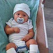 Messiah is registered to the contest to win money with this photo: baby, infant, child, pacifier, hat, striped_clothing, onesie, socks, bouncer, baby_chair, indoor, portrait, sitting, lying_down, cozy, turquoise, adult, legs, face, home