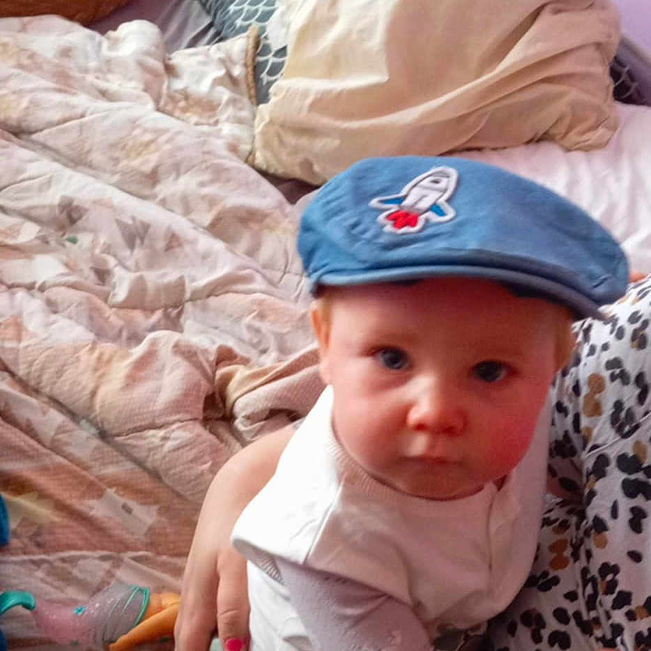 Aaron a rejoint le concours — aidez-le/la à gagner de superbes lots ! animal, baby, bed, blanket, cap, cat, child, clothing, curious, cute, hand, holding, home, indoor, infant, leopard_print, person, pillow, rocket_patch, sitting