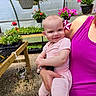 baby, child, person, flower, greenhouse, plants, hanging_plants, potted_plants, pink_clothing, magenta_clothing, smiling, happy, indoor, nature, garden, holding, portrait, cute, infant, colorful