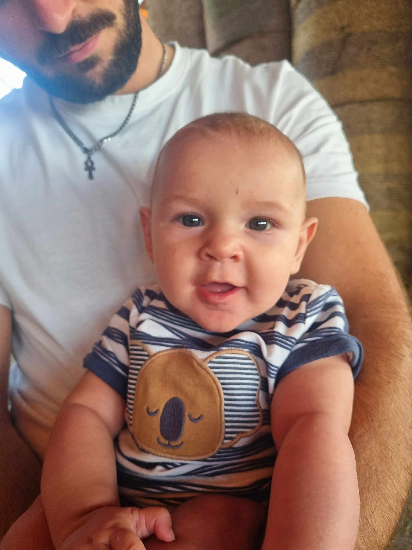 Ezéchiel participe au concours pour gagner de l'argent avec cette photo : baby, man, beard, smiling, holding, indoor, striped_shirt, koala_patch, white_tshirt, portrait, happy, child, person, closeup, arm, casual_clothing, face, infant, seated, family