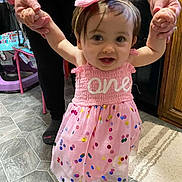 Amiya is registered to the contest to win money with this photo: toddler, child, pink_dress, headband, bow, holding_hands, adult, kitchen, floor_tiles, rug, walking, happy, indoor, person, footwear, confetti_pattern, smiling, baby, celebration, assistance