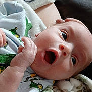 Oakley is registered to the contest to win money with this photo: baby, infant, newborn, blanket, onesie, clothing, surprised, mouth_open, wide_eyes, face, hand, couch, furniture, soft_texture, pattern, close_up, portrait, indoors, skin, lying_down