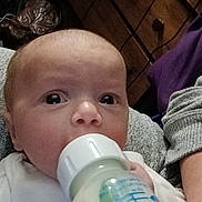 Oakley is registered to the contest to win money with this photo: baby, bottle, feeding, milk, infant, person, face, hand, clothing, furniture, drawer, wood, indoor, closeup, newborn, expression, sitting, adult, casual, portrait