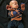 baby, infant, striped_hoodie, mittens, black_pants, bare_foot, lying_down, curious_expression, face, head, clothing, child, young, portrait, indoor, person, cute, small, newborn, apparel