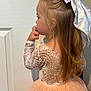 bow, child, cute, dress, fashion, girl, hair, hand_to_mouth, indoor, lace, long_hair, peach_color, person, portrait, side_view, skirt, thinking, tulle, white_door, young_child