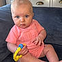 baby, child, infant, blue_eyes, pink_onesie, toy, couch, furniture, drool, curious, sitting, indoor, wooden_cabinet, diffuser, device, blue, yellow, hand, foot, face