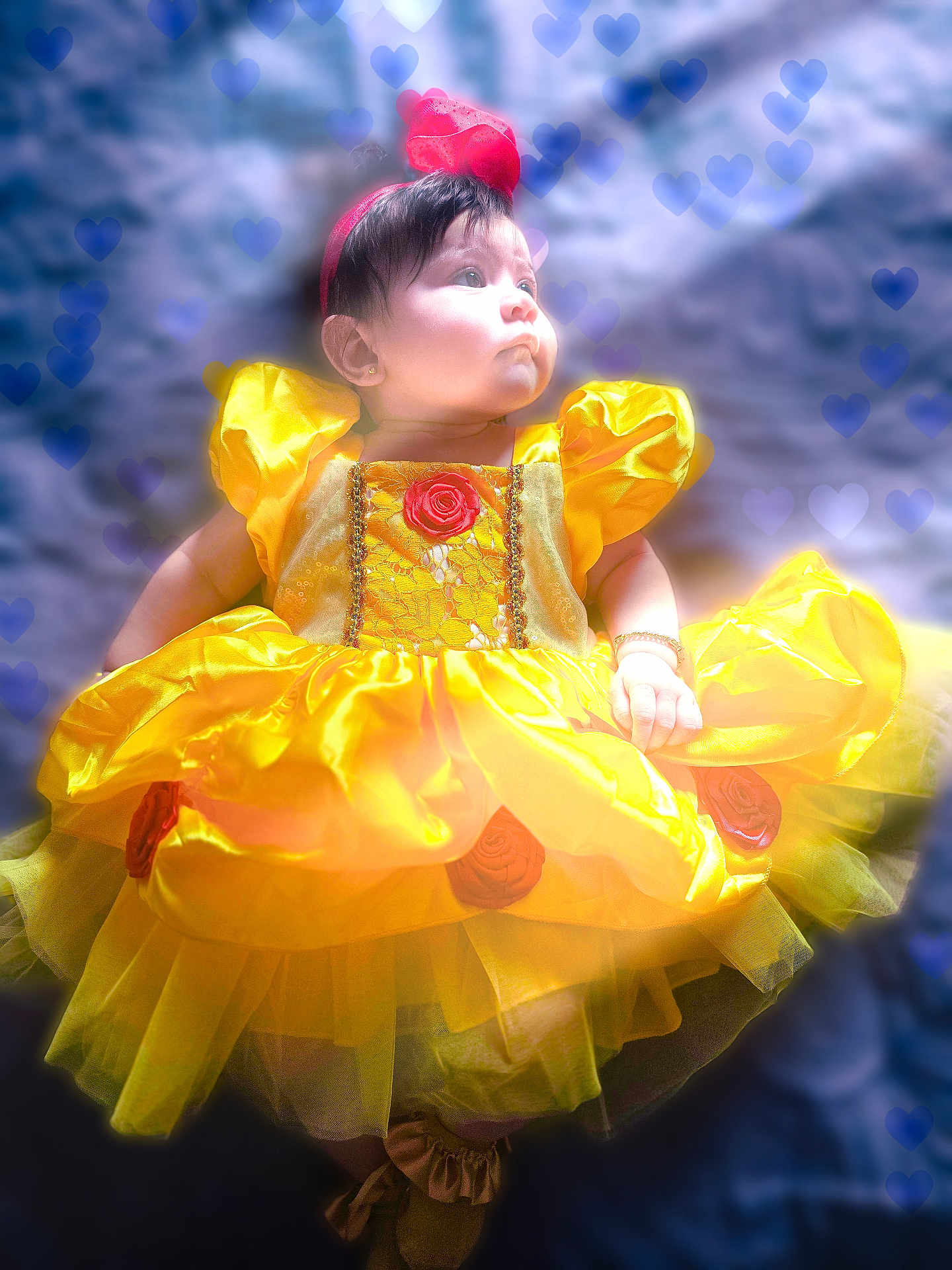 Jeannine is registered to the contest to win money with this photo: baby, child, dress, yellow_dress, red_headband, heart_overlay, cute, portrait, infant, soft_lighting, blue_background, puffed_sleeves, tulle_skirt, earrings, bracelet, lying_down, adorable, costume, fabric, face