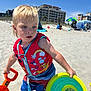 child, toddler, beach, sand, shovel, frisbee, life_vest, sunny, blue_sky, shorts, barefoot, toy, outdoor, vacation, summer, building_sandcastles, playing, colorful, water_toys, daytime