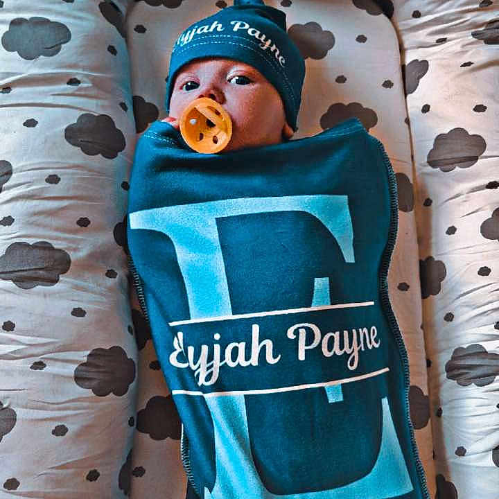 Elyjah is registered to the contest to win money with this photo: baby, baby_nest, blanket, blue, child, cloud_pattern, comfort, cozy, cute, hat, indoors, infant, newborn, pacifier, person, portrait, resting, sleeping_area, soft_fabric, swaddle