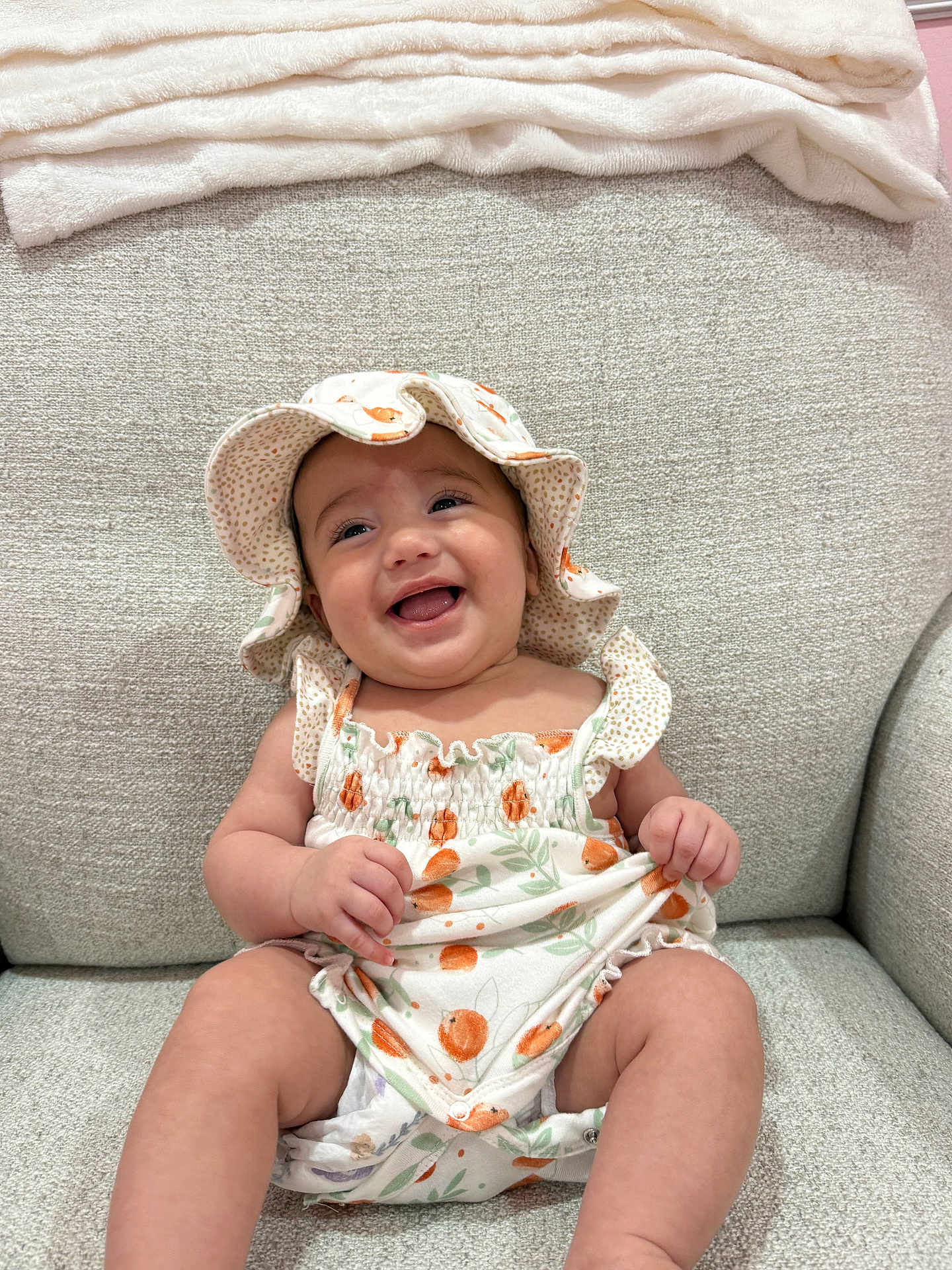 Juliette is registered to the contest to win money with this photo: baby, smiling, hat, romper, orange_pattern, green_leaves, sitting, couch, beige, soft_texture, happy, infant, child, cute, indoor, clothing, portrait, face, person, toddler