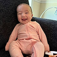 Juliette joined the competition — help win amazing prizes! baby, smiling, pink_onesie, polka_dots, chair, indoor, happy, infant, cozy, blanket, pattern, texture, natural_light, cute, portrait, child, seated, warmth, comfortable, expression