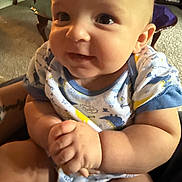 Brian is registered to the contest to win money with this photo: baby, child, infant, smiling, portrait, close_up, face, eyes, indoors, seated, onesie, clothing, hands, arms, chair, carpet, furniture, home, warm_lighting, photography