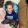 Blue joined the competition — help win amazing prizes! person, dog, sleeping, couch, blanket, pillow, blue, black_dog, white_spots, relaxing, indoors, casual_clothing, basketball_shirt, hair_tied, resting, cozy, carpet, cord, patterned_fabric, comfort