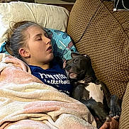 Blue is registered to the contest to win money with this photo: person, dog, sleeping, blanket, couch, indoor, cozy, resting, comfort, relaxation, snuggling, pet, animal, human, casual, blue_shirt, brown_couch, pillow, fur, nap