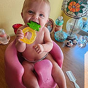Xoie joined the competition — help win amazing prizes! baby, infant, teether, pink_seat, wooden_table, lamp, stained_glass, decorative_items, glass_containers, photo_frame, cow_figurines, comb, smiling, chewing, cute, indoors, child, toy, happy, person