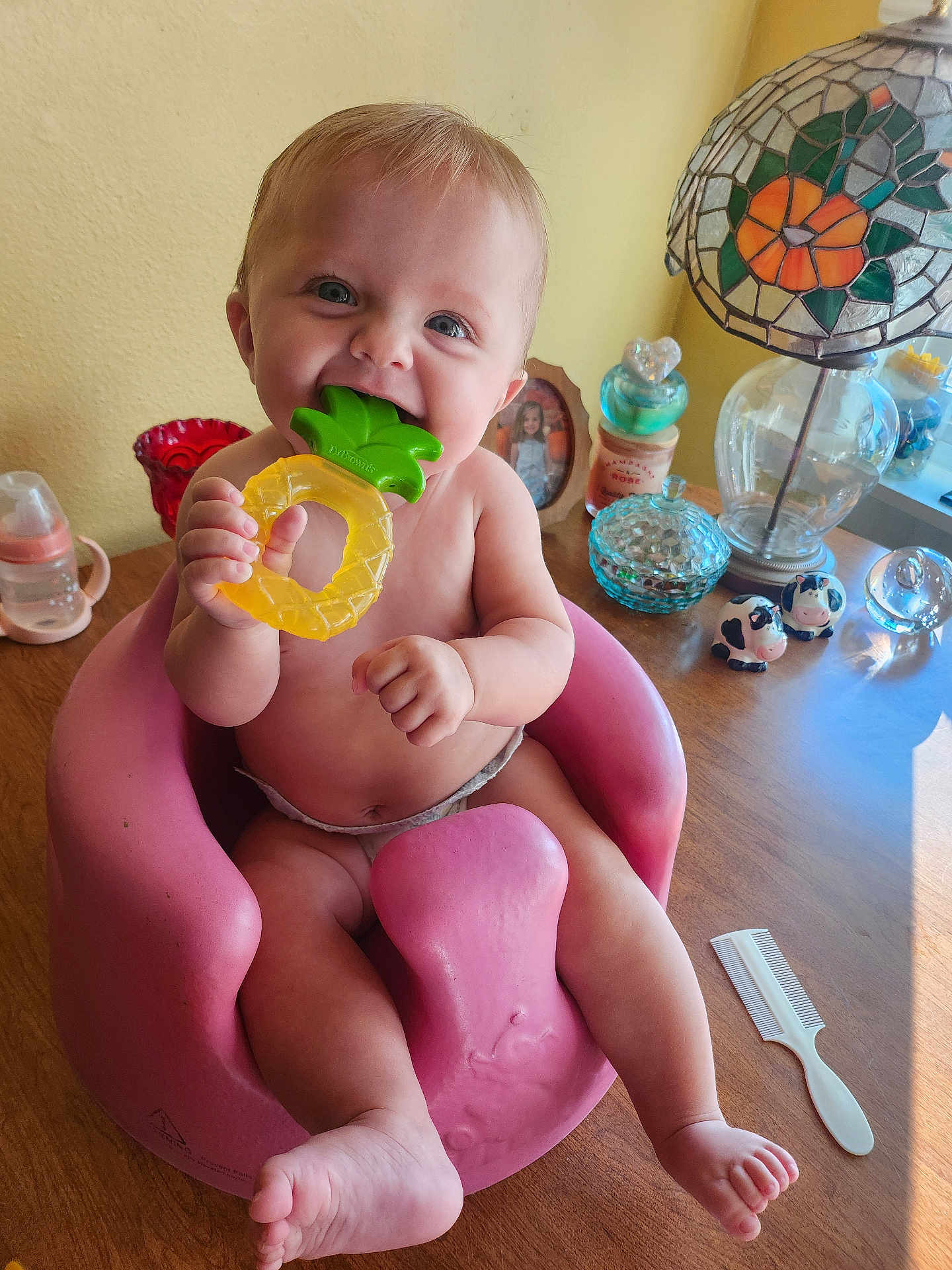 Xoie joined the competition — help win amazing prizes! baby, infant, teether, pink_seat, wooden_table, lamp, stained_glass, decorative_items, glass_containers, photo_frame, cow_figurines, comb, smiling, chewing, cute, indoors, child, toy, happy, person