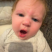 Rose is registered to the contest to win money with this photo: baby, child, face, blue_eyes, light_hair, expression, open_mouth, couch, quilted_cushion, ribbed_shirt, indoor, portrait, close_up, sitting, person, young_child, infant, skin, head, eyebrows