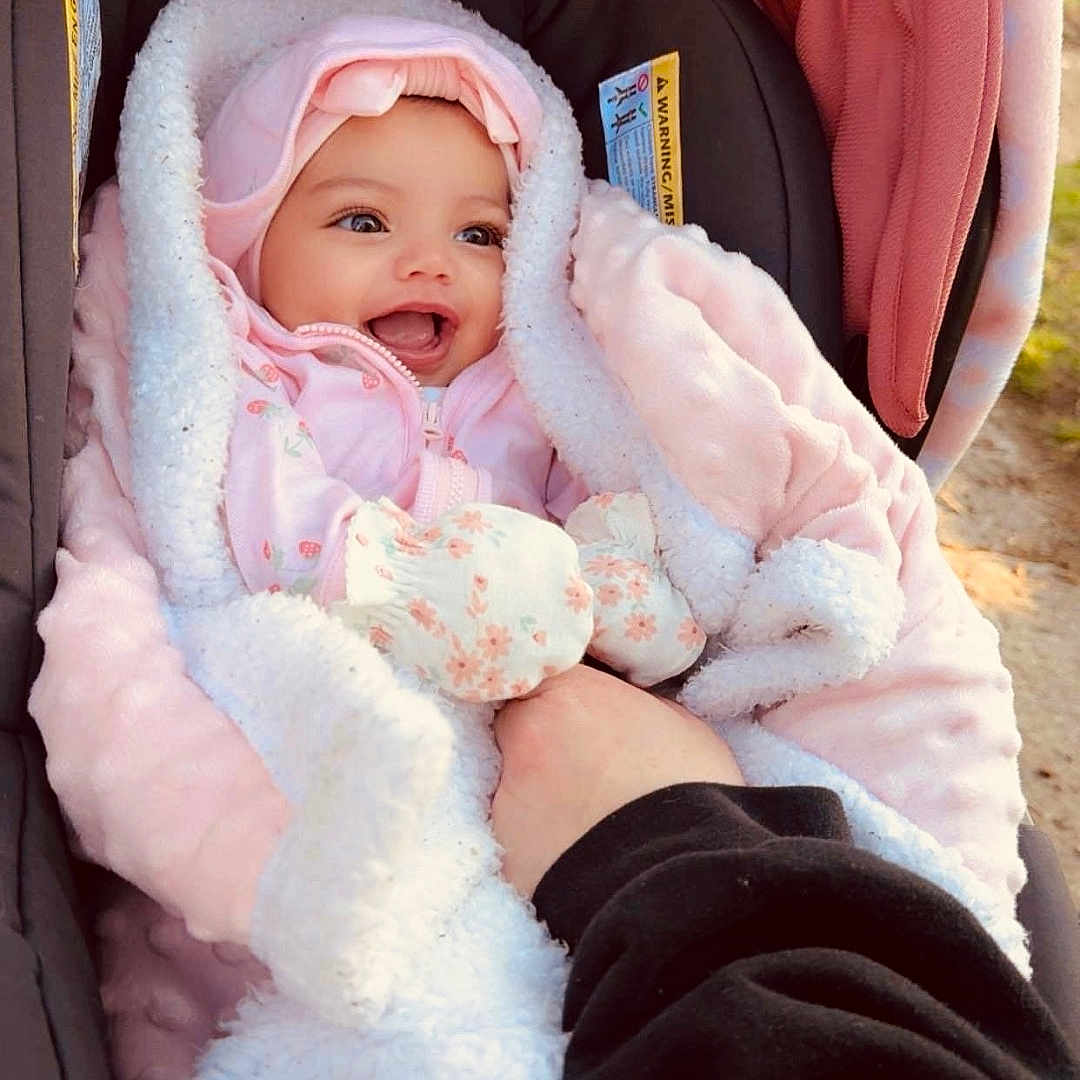 Kaylani joined the competition — help win amazing prizes! baby, infant, car_seat, blanket, pink, mittens, smiling, face, person, cute, warm_clothing, hood, hand, cozy, outdoor, child, apparel, happy, portrait, newborn