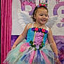 child, girl, smiling, fairy_wings, tutu, colorful_dress, flower_crown, curly_hair, stage, costume, party, celebration, pink, purple, blue, green, glitter, happy, portrait, event