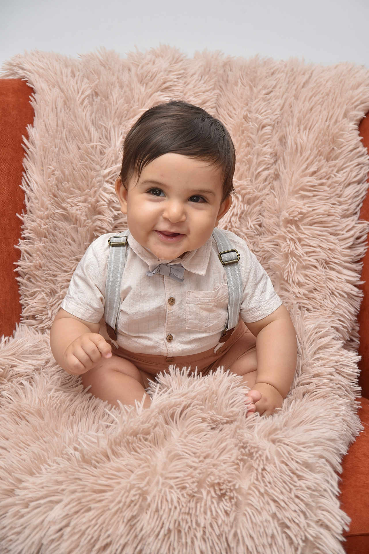 Yassine a rejoint le concours — aidez-le/la à gagner de superbes lots ! baby, child, smile, face, shirt, bow_tie, suspenders, fluffy_blanket, chair, indoor, cute, portrait, happy, infant, soft_texture, plush, seated, person, candid, adorable