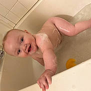 Elijah is registered to the contest to win money with this photo: baby, bath, bathtub, water, foam, rubber_duck, child, smile, skin, hand, face, happy, playing, splash, tiled_wall, faucet, soap_bubbles, bath_time, infant, cute