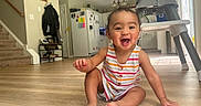 Anastasia is registered to the contest to win money with this photo: baby, child, smiling, indoor, floor, wooden_floor, striped_clothing, high_chair, kitchen, home, staircase, cabinet, refrigerator, light, person, happy, sitting, infant, cute, portrait