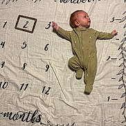 Colby is registered to the contest to win money with this photo: baby, infant, onesie, milestone_blanket, months, numbers, wooden_frame, lying_down, curious, cute, child, fabric, leaf_design, age_marker, sleepwear, indoors, portrait, person, small_child, soft_texture