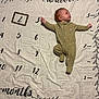 baby, infant, onesie, milestone_blanket, months, numbers, wooden_frame, lying_down, curious, cute, child, fabric, leaf_design, age_marker, sleepwear, indoors, portrait, person, small_child, soft_texture